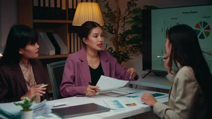 Poster - Three asian businesswomen are working late in the office. They are discussing a finance report and pointing at charts on the table