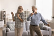 © fizkes - Happy carefree retired 60s couple dancing in cozy living room, enjoy active pastime and hobby, spend lively weekend leisure together at modern home, moving, listening favourite music feel overjoyed
