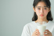 © smth.design - Concerned young Asian woman holding a glass of milk against a neutral background