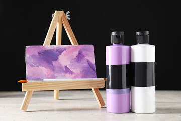 Poster - Acrylic paints of different colors in bottles, brush and small easel with abstract picture on light table