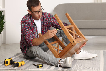 Canvas Print - Man repairing wooden stool with screwdriver indoors