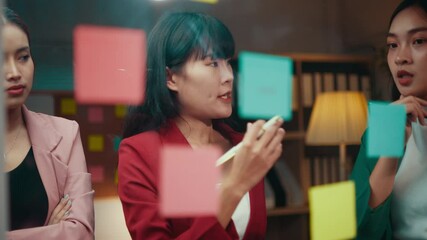 Poster - Team of young businesswomen is having a discussion in their office. They are using sticky notes on a glass wall to brainstorm