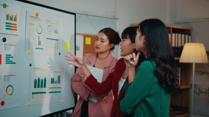 Poster - Three businesswomen having a discussion about marketing data on a whiteboard. One businesswoman is pointing at the board while the others are listening attentively