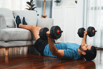 Wall Mural - Athletic body and active sporty man using furniture for effective targeting muscle gain with weight lifting dumbbell exercise at gaiety home as concept of healthy fit body home workout lifestyle.