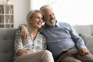 Pretty aged spouses sit on sofa, laughing looking into distance having optimistic mood, daydreaming about bright future, enjoy their strong marriage and good warm harmonic relationship. Love, marriage