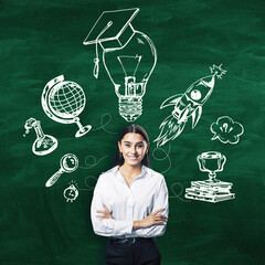 Confident businesswoman standing in front of a chalkboard with education and success concept icons drawn on it.