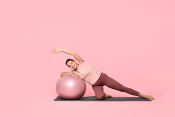 Wall Mural - Beautiful pregnant woman with fitball doing exercises on mat against pink background