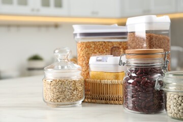 Wall Mural - Different types of cereals and legumes in containers on white marble table in kitchen, closeup