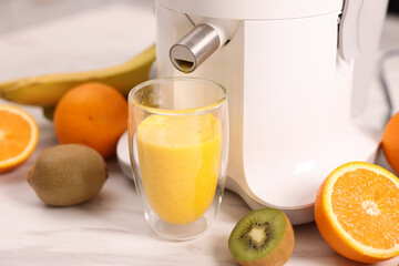 Modern juicer, fresh fruits and glass on white marble table in kitchen, closeup