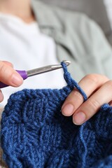 Wall Mural - Woman crocheting with hook and blue yarn, closeup