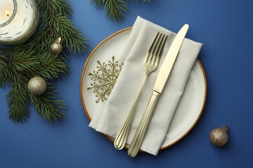 Poster - Beautiful Christmas setting with plate, elegant cutlery and festive decor on blue table, flat lay