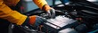© Elmira - A mechanic carefully attends to an electric vehicle's battery, wearing gloves and a bright yellow jacket, in a well-equipped automotive workshop