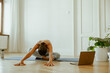 © Viktoria Kovalchuk - A woman practices yoga at home using a laptop and stays hydrated with a water bottle