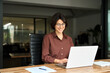© insta_photos - Busy young business woman executive using laptop in office. Smiling Hispanic businesswoman company employee sitting at work desk, professional female hr manager looking at pc computer at workplace.