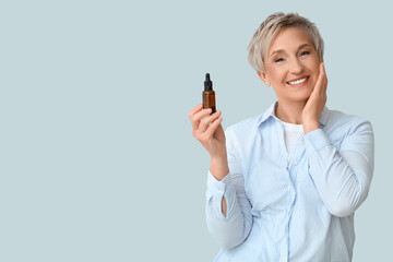 Wall Mural - Mature woman with bottle of serum on light background