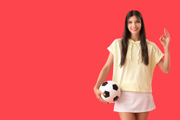 Wall Mural - Young woman with soccer ball showing OK on red background