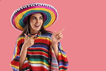 Wall Mural - Beautiful woman in traditional Mexican clothes showing something on pink background