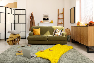 Interior of living room with green sofa and fallen leaves