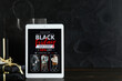 © Pixel-Shot - Tablet computer with Black Friday fashion sale advertisement, gift boxes and shopping bag on dark grunge background