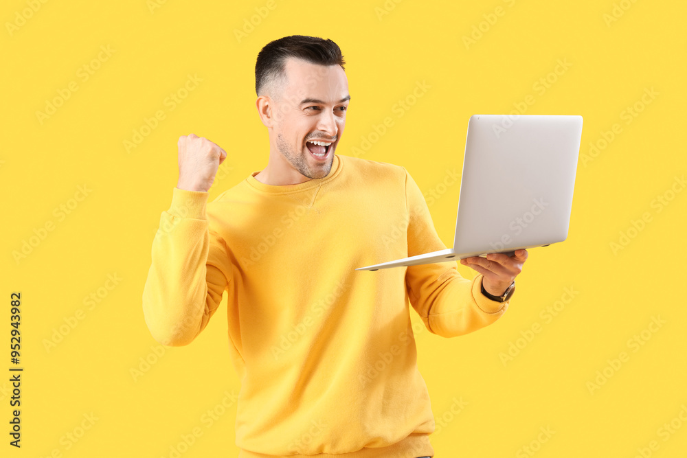 Happy young man with laptop on yellow background