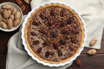 Poster - Delicious pecan pie in baking dish and fresh nuts on wooden table, flat lay