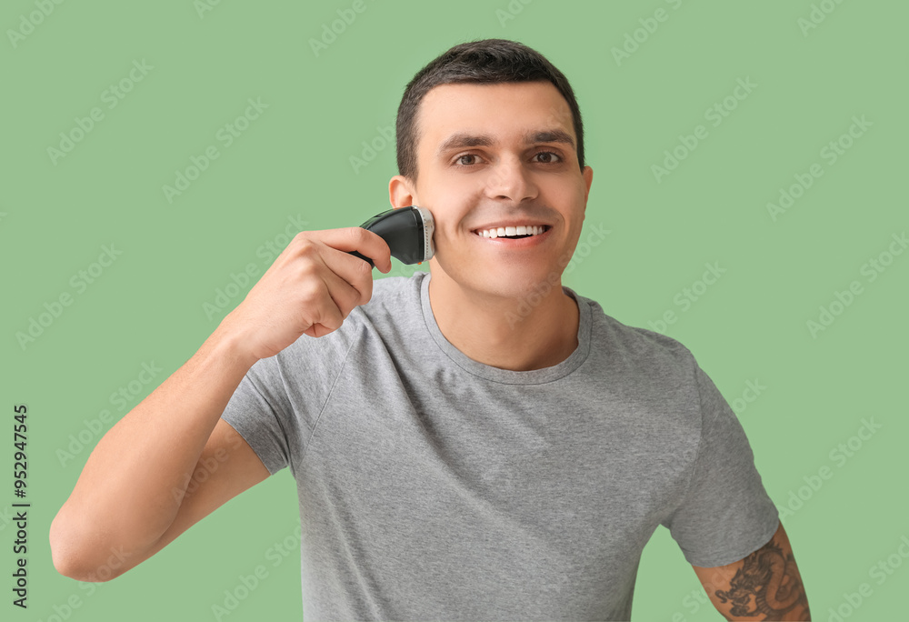 Handsome young man with electric shaver on green background