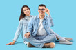 © Pixel-Shot - Young couple in eyeglasses sitting on blue background
