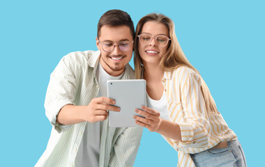 Poster - Young couple in eyeglasses using tablet computer on blue background