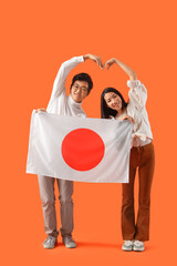 Poster - Young Asian couple with flag of Japan making heart gesture on orange background