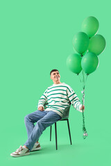 Poster - Young man with bunch of balloons sitting on chair against green background