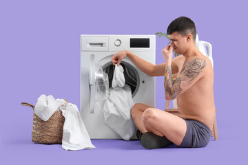 Wall Mural - Young man in underpants with stinky socks doing laundry on lilac background