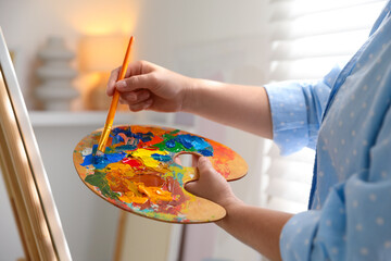 Canvas Print - Woman mixing paints on palette with brush near easel indoors, closeup