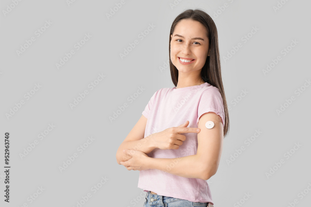 Diabetic young woman pointing at glucose sensor on light background