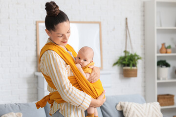 Beautiful young happy mother with cute little baby in sling at home