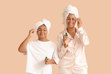 Canvas Print - Happy young African-American mother and her daughter in pajamas applying cosmetic oil on beige background