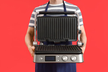 Wall Mural - Young man with modern electric grill on red background, closeup