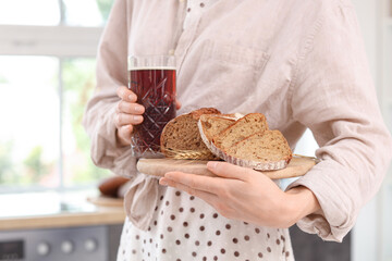 Wall Mural - Young woman with glass of tasty kvass and bread slices in kitchen, closeup