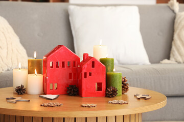 Burning candles with house shaped holders and Christmas decor on table in living room, closeup