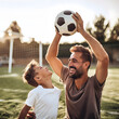 © mindstorm - Father and son having fun together playing with a soccer ball on a sunny day in a suburban environment