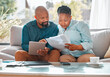 © Nina2024/peopleimages.com - Documents, finance and tablet with mature black couple on sofa in living room of home for wealth management. Bank, investment or savings with man and woman in apartment for budget or pension planning