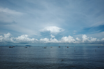 A serene coastal scene featuring a wide expanse of calm sea with scattered fishing boats gently floating on the water in Chon buri, Thailand.