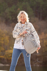 a tall blonde girl with a backpack enjoys the autumn views of nature, forest and lake in the mountains. young woman traveling