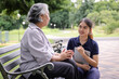 © kamonrat - Young caregiver discussing senior care plans with an elderly woman using a laptop while sitting on a park bench, emphasizing attentive support and personalized elderly care in a serene environment.