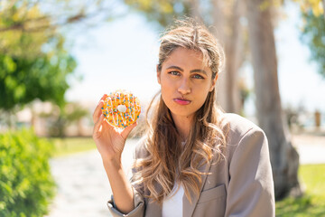 Poster - Pretty blonde Uruguayan woman holding a donut at outdoors with sad expression