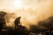 © Josu - Worker at a landfill site in a cloud of dust during sunrise.