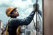 © Josu - African female worker in her 30s cleaning windows on a high-rise building.