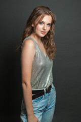 Brunette young adult woman in silk top wearing light jacket standing against black studio wall background