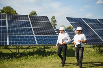 Solar power plant with two engineers walking and examining photovoltaic panels. Concept of alternative energy and its service