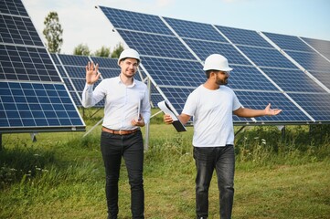 Wall Mural - Solar power plant with two engineers walking and examining photovoltaic panels. Concept of alternative energy and its service