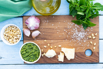 ingredients for the preparation of pesto sauce. basil, pine nuts, garlic, basil, parmesan on a blue table and wooden board